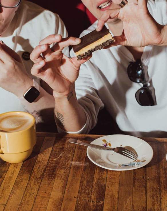 Two people eating Nanaimo bars with lattes.