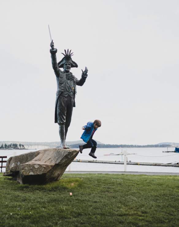 A kid jumping from a rock with a statue onto the grass.