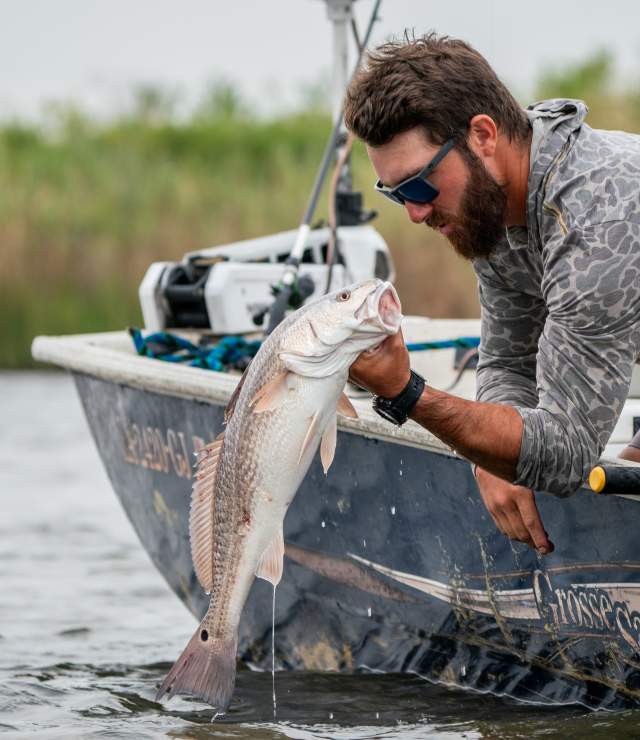 Angler aboard a fishing boat near marsh wetlands in Southwest Louisiana holding a redfish above the water during a guided fishing trip at Grosse Savanne.