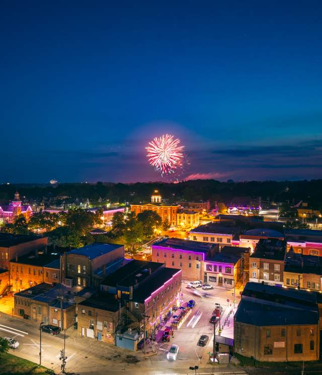 A bright orange firework popping in the night sky with a aerial view of the square.