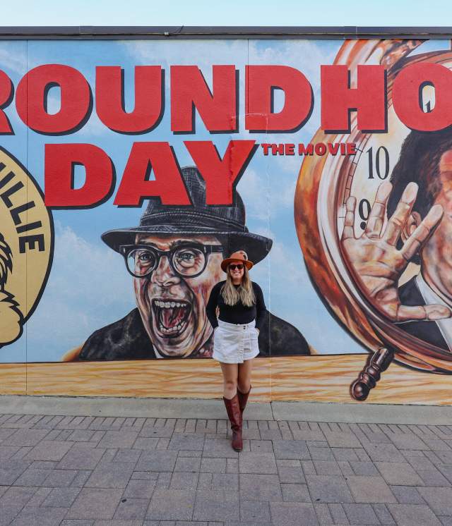Woman stands in front of mural of Woodstock Groundhog Days in Woodstock, IL