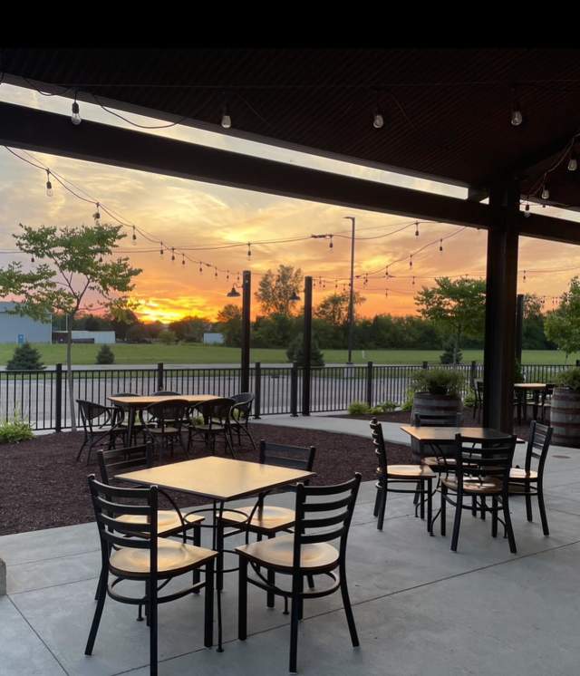 picture of a pink and peach sunset while on a patio with tables and chairs and string lights.