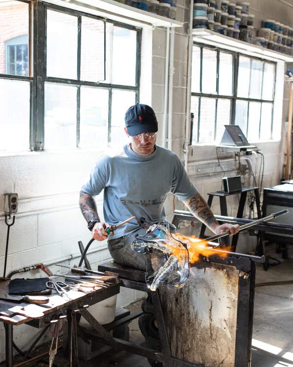Man is torching a handmade piece of glass that is to be made into a bowl