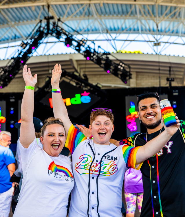 three friends cheering in front of a stage at pridefest