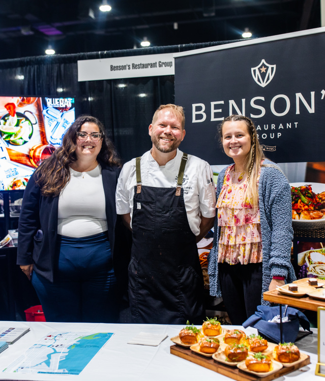 woman, man, and another woman smiling at a booth displaying lobster rolls and smores pie