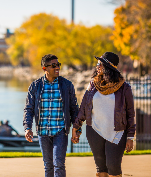 a couple walking and holding hands with fall foliage in the background