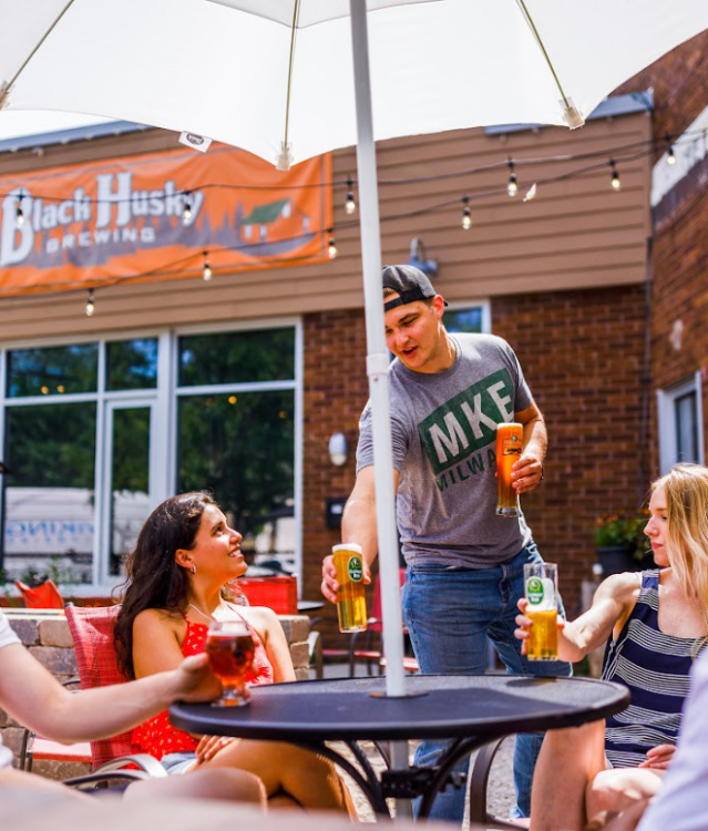 friends gathered around table outside of Black Husky Beer