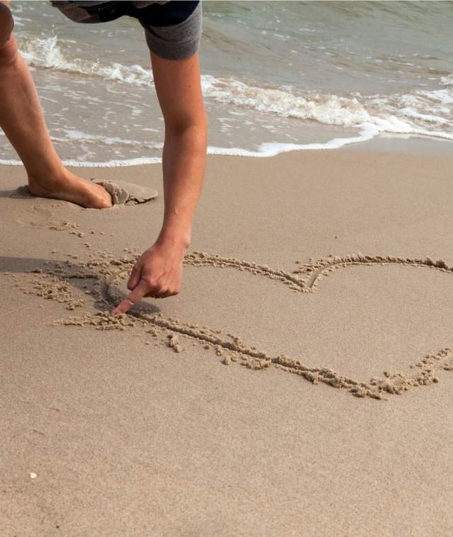 Someone drawing a heart in the sand on a beach