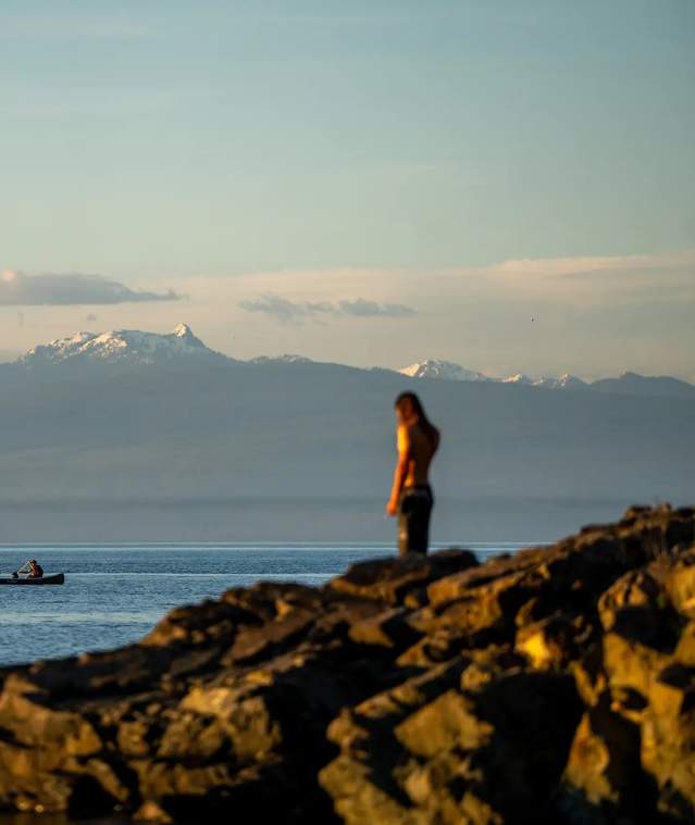 A person standing on rocks looking at a boat on the ocean.