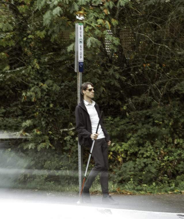 A blind man waiting at a bus stop.