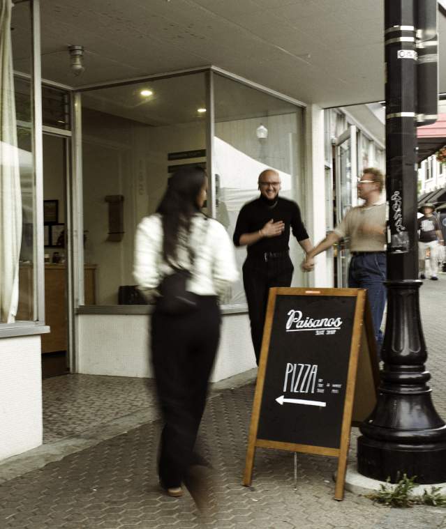 A welcoming moment outside a Nanaimo café and pizza shop, with people chatting and walking along a busy downtown sidewalk.