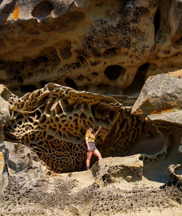 An individual stands against a wall of unique sandstone formations.