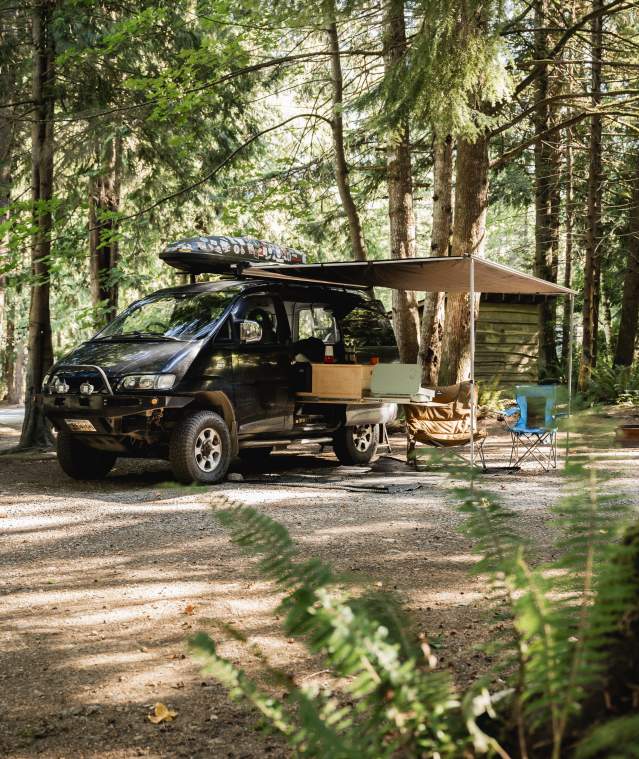 A camper van set up with a tent and chairs.