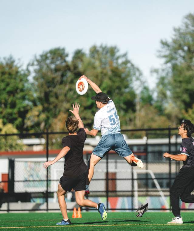 People playing ultimate frisbee as one player jumps into the air to catch the frisbee.
