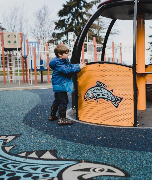 A young boy at a playground look at a merry go round.