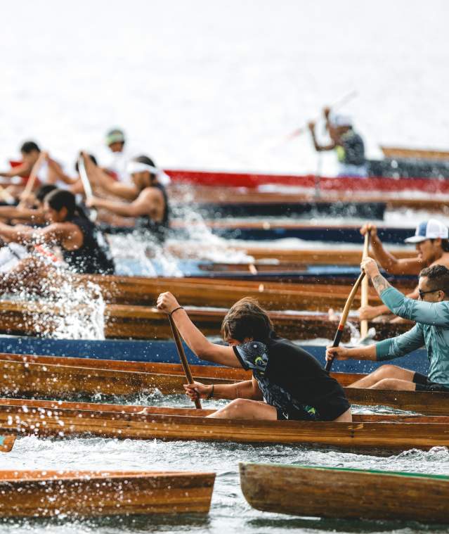 People racing traditional wooden canoes on the water.