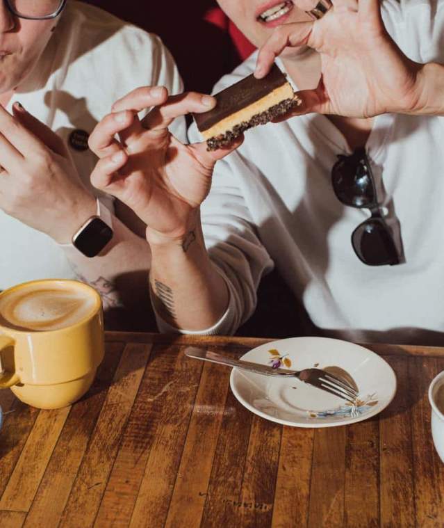 Two people eating Nanaimo bars with lattes.