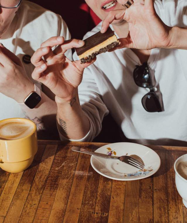Two people eating Nanaimo bars with a latte.