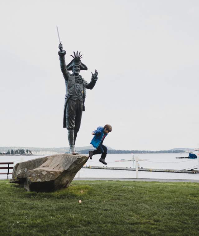 A kid jumping from a rock with a statue onto the grass.