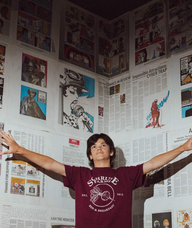 A person standing with their arms out in front of a wall covered in newspaper.