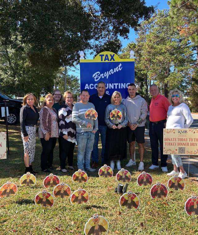 Group of people surrounded by a display of cardboard turkey cut-outs in front of a local business.