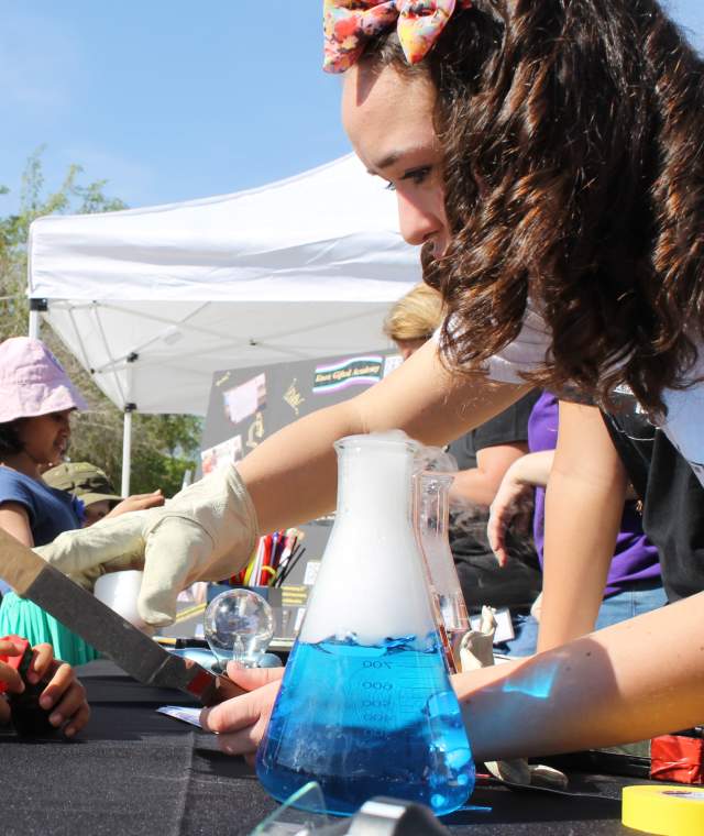 a young boy at an event table is watching a science demonstration