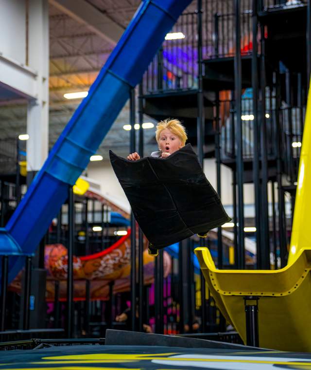Kid on mat in a mid air jump from sliding down slide ramp.