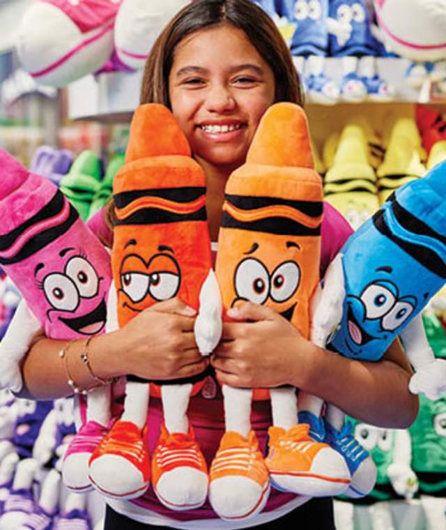 Girl smiling hugging colorful crayon plushies.