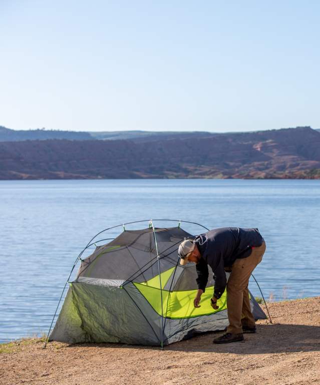 he back of a camper setting up a tent along a shoreline.