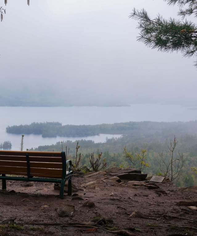 A bench on the summit of The Pinnacle facing a foggy view of Lake George and Adirondack Mountains