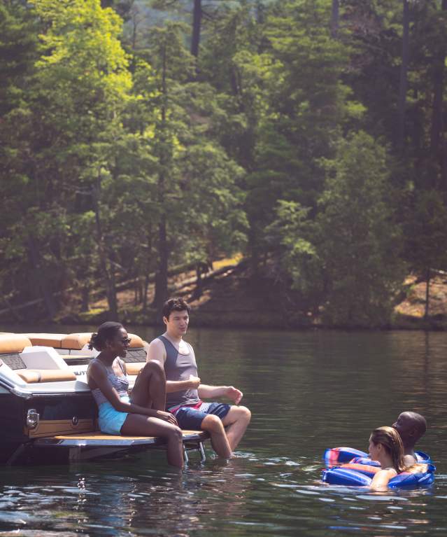 Friends sitting on the back of a boat and swimming in Lake George