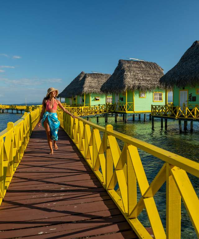 Mulher caminhando por um píer com bangalôs sobre a água em Bocas del Toro, Panamá.