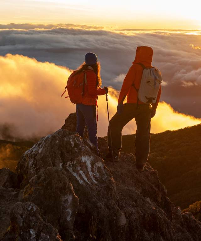 Hikers watching the sunrise from the summit of Volcan Baru, surrounded by clouds and mountainous landscapes in Panamá.
