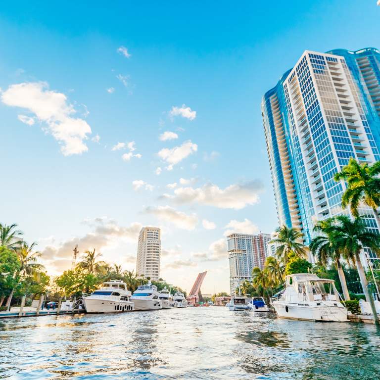 A view from the New River of yachts and high rises with a very blue sky and some puffy clouds
