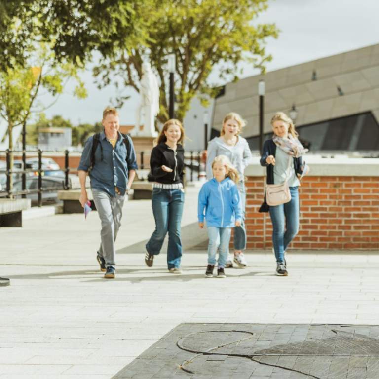 Family walking along Hull’s waterfront near The Deep, passing a large stingray sculpture embedded in the pavement on the Hull Fish Trail, with modern architecture and open public space creating a lively sightseeing atmosphere