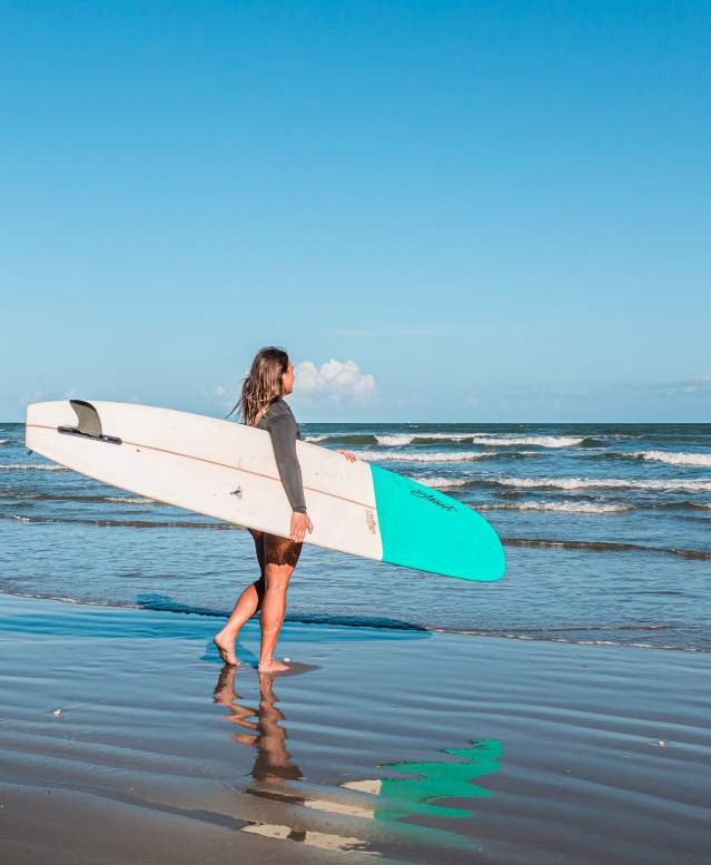 Girl holding a white and blue surf board walking into the water.