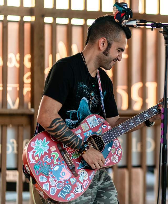 A guitarist rocks out with a red guitar covered in stickers.