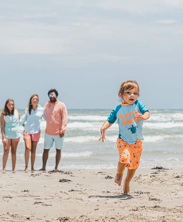 A family watches a toddler run across the beach in Port Aransas, Texas