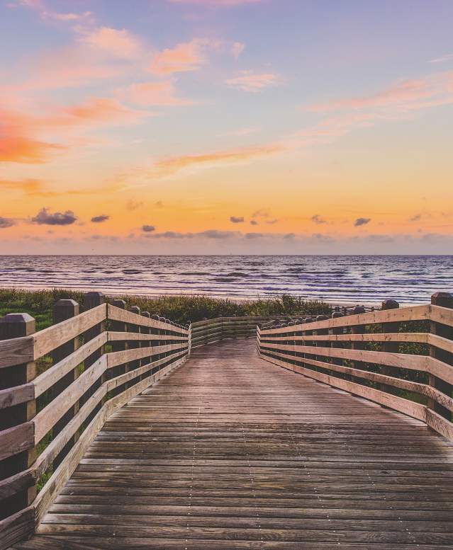 A wooden boardwalk leading to the beach at sunrise