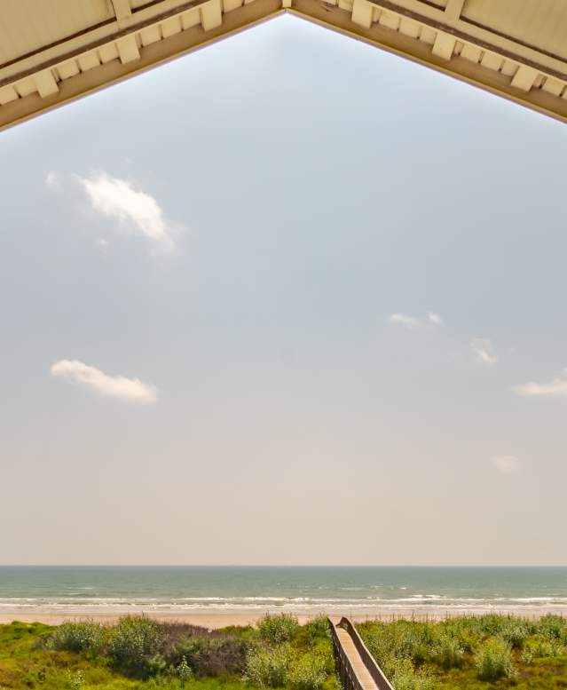 A view off a porch of Port Aransas over looking the beach and a boardwalk.