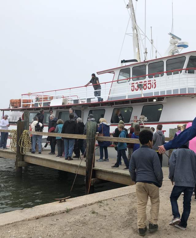A group of kids and adults waits in line to board a large white boat