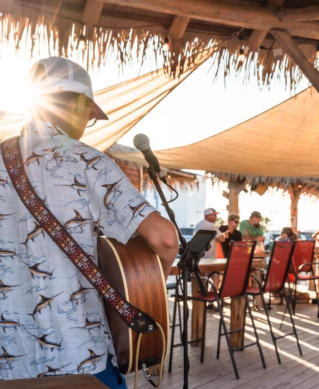 Photo from behind a musician playing guitar towards a tiki bar