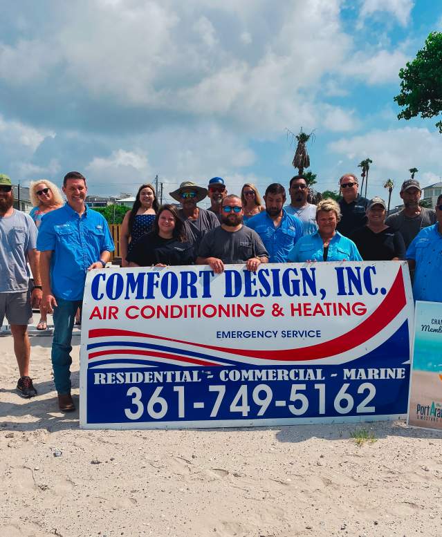 A group of people stand behind and around a large red, white, and blue sign reading "Comfort Design, Inc" with other details of the business below.