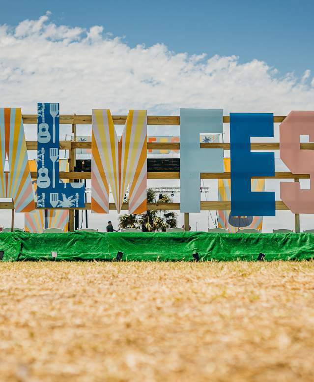Up close shot of a large sign in the style of the Hollywood sign that reads "PalmFest." Each letter is painted in a different coastal pattern or color.