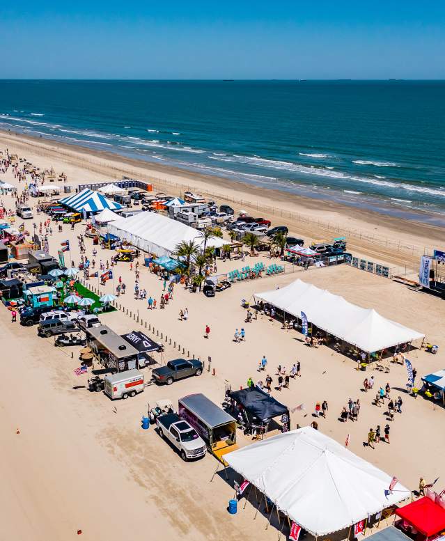 Aerial shot of a long stretch of beach covered in tents and people during a festival.