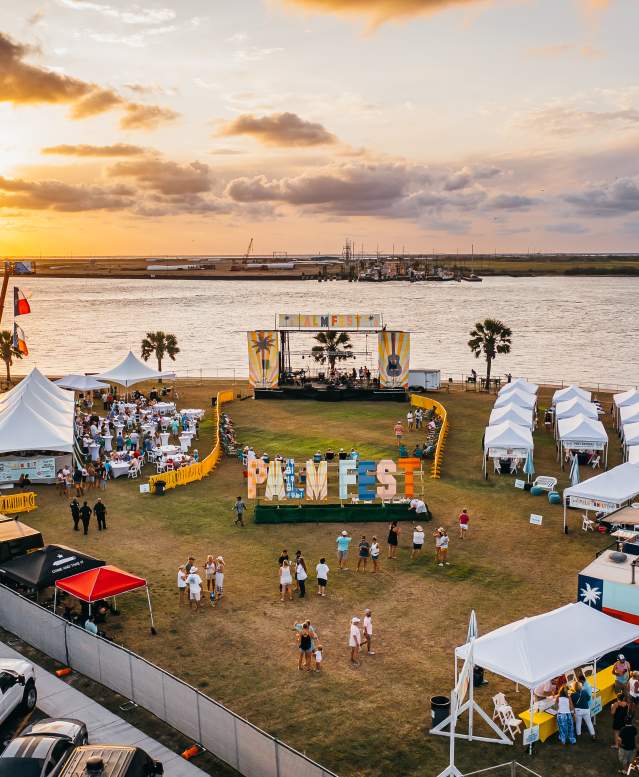 Aerial view of a park right on the ship channel. In the park are tents, a music stage, people, and a large sign reading "PalmFest."