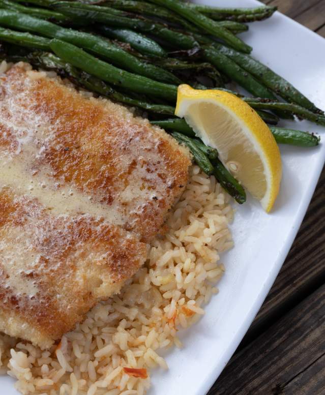 A plate of fried fish with green beans and a lemon sits on a wooden tabletop