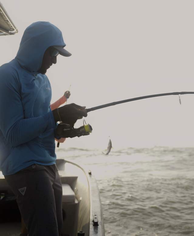 A man in Columbia PFG gear holds a bent fishing pole on a boat.