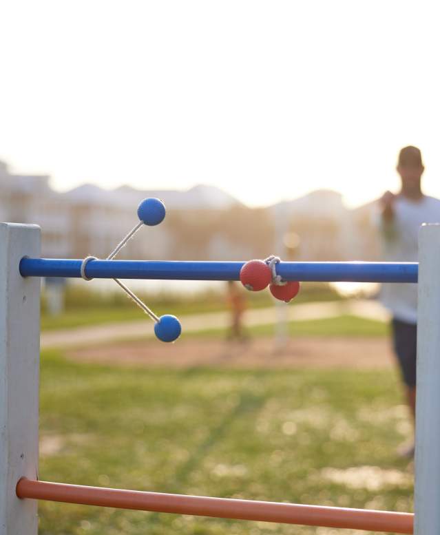 A blue ladder ball wraps around the top wrung next to a red already wrapped around. The man who threw the ladder ball is out of focus in the back