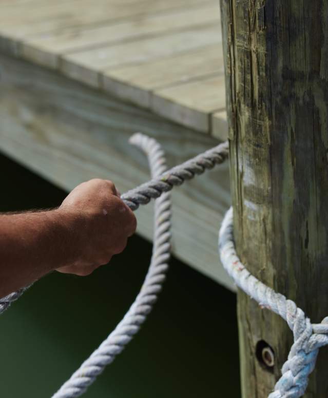 Hands are in the act of tying a white marine rope around a wooden dock pole
